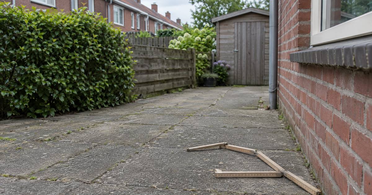 Een houten duimstok ligt opengevouwen op de tegels van een achtertuin, naast de rode bakstenen muur van het huis. Illustratie.
